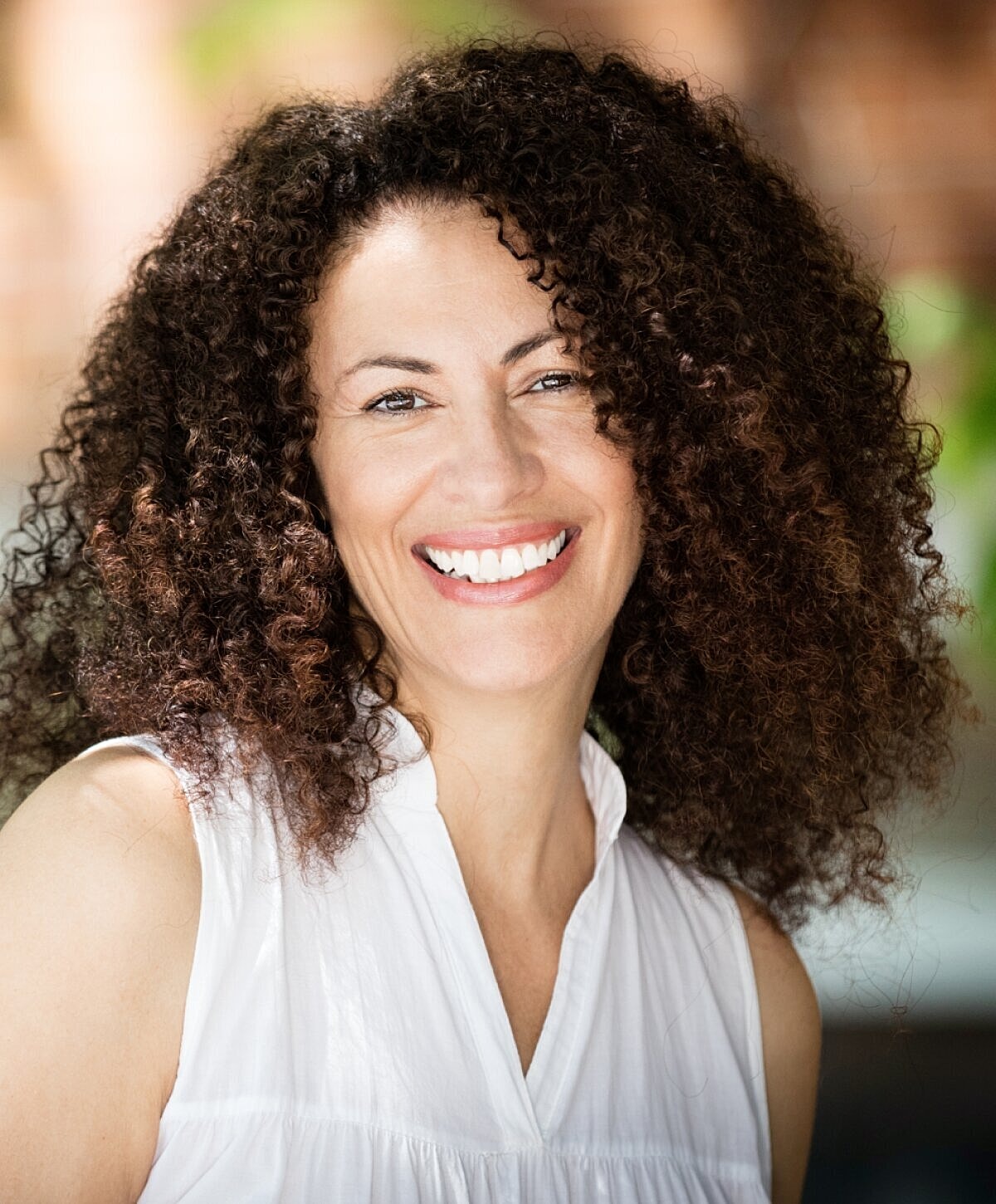 Smiling woman with curly hair wearing white shirt.